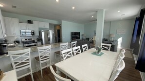 A modern kitchen with white cabinets, a dining area with white chairs, and a central island. - Family Seaclusion - Oceanfront in Garden City Beach (Garden City Beach)