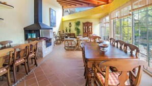 A spacious dining area with a high ceiling, wooden beams, and large windows offering a view of the outdoors.