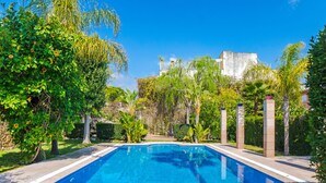 A rectangular swimming pool with a clear blue water surface, surrounded by lush greenery and a stone wall.