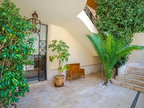 Um espaço amplo e interno com um banco de madeira, plantas em vasos e uma escada que leva a um andar superior.