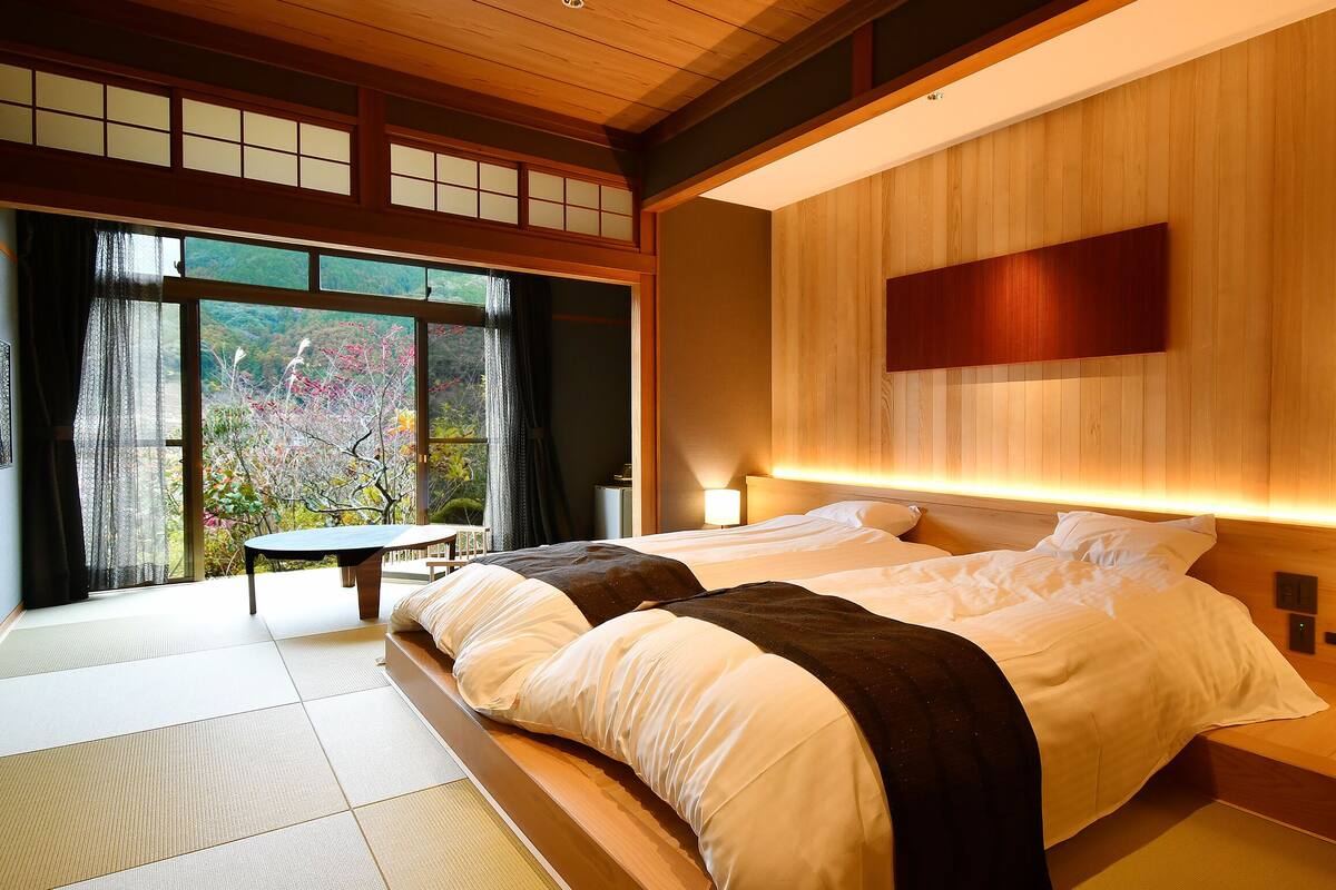 A hotel room with a large bed, bedside tables, a view of the outdoors, and traditional Japanese sliding doors.