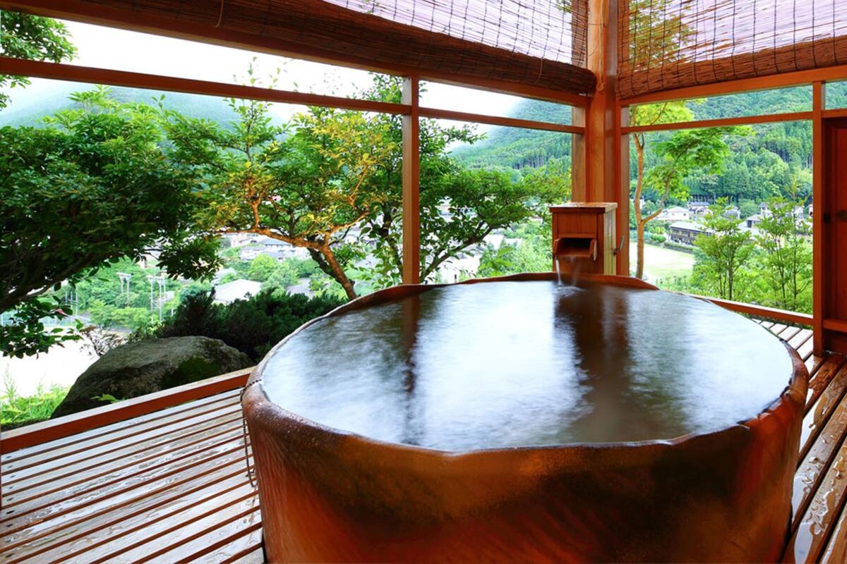 A wooden hot tub on a deck with a view of a forested area.