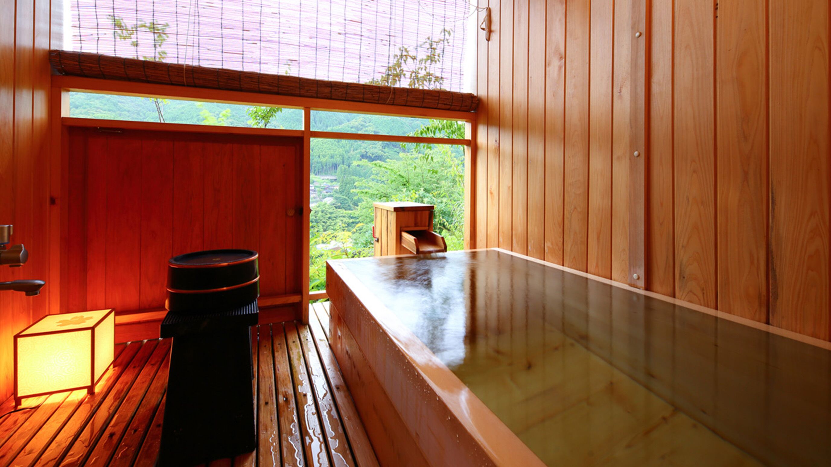 Una stanza in legno con una vasca idromassaggio, uno sgabello di legno e una finestra vista verde.