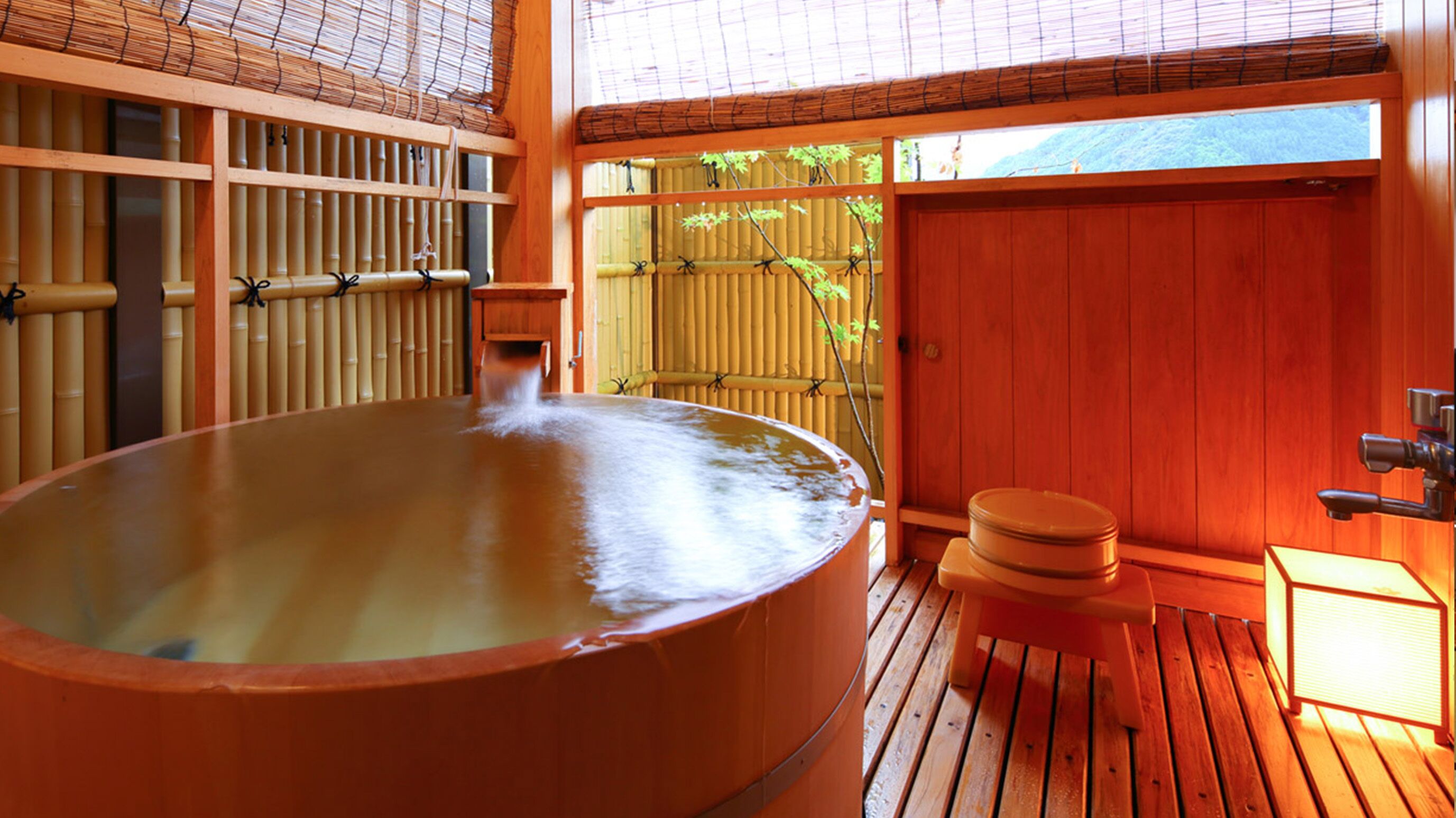 Bagno termale con una veranda in legno, pareti di bambù e vista sulla vegetazione.