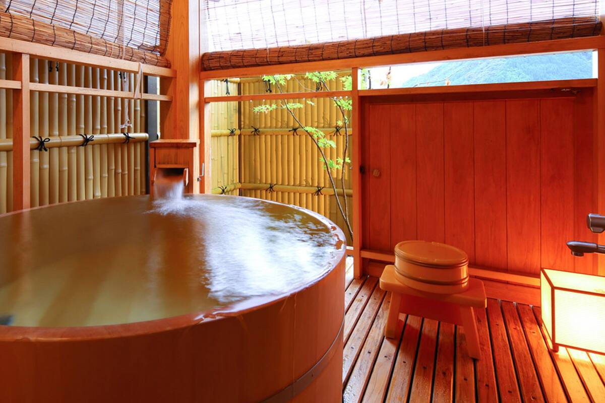 A hot spring bath with a wooden deck, bamboo walls, and a view of greenery outside.