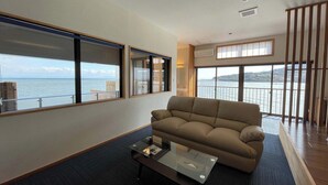 Uma sala de estar moderna com um sofá, uma mesa de centro de vidro e amplas janelas com vista para o mar.