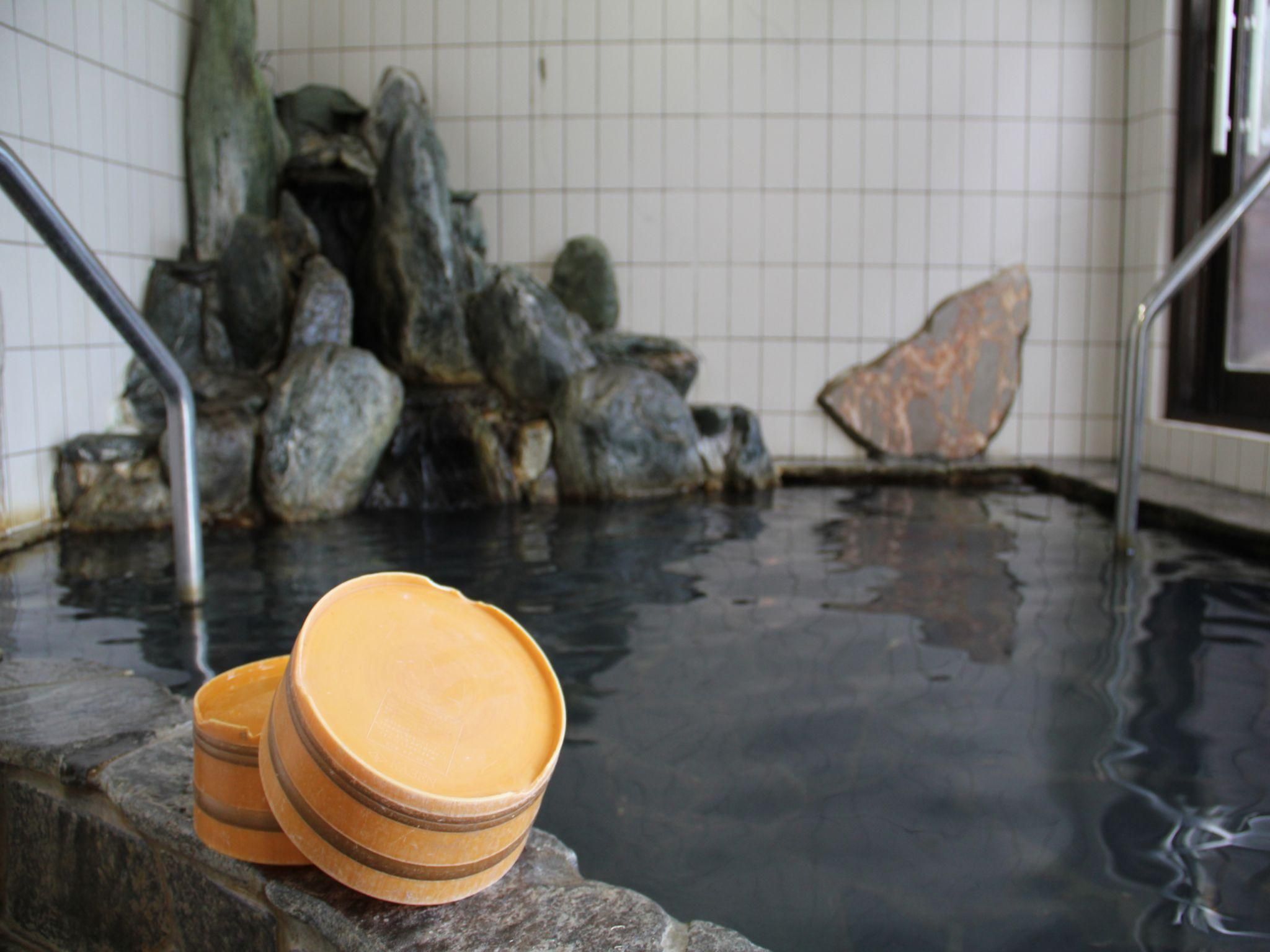 Un área de aguas termales con escalones de piedra que bajan al agua, barandillas metálicas y una pared de azulejos al fondo.