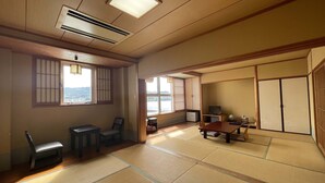 Um quarto japonês tradicional com tatames, uma mesa baixa com cadeiras, uma televisão e portas deslizantes.