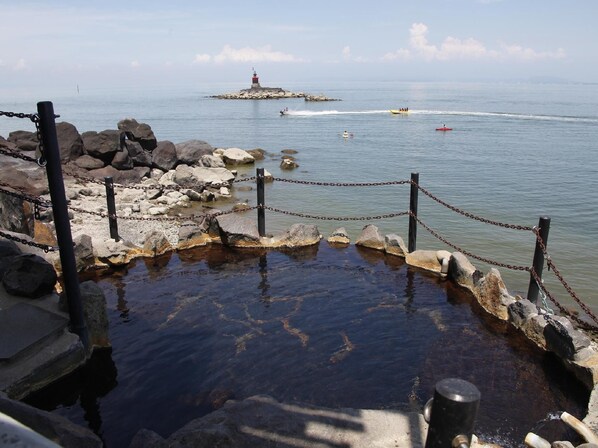 A rocky shoreline with a chain barrier, a lighthouse in the distance, and a body of water. - Tara Kanko Hotel (Tara)