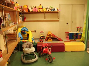 A playroom with a baby walker, a tricycle, and various toys on shelves. - Tara Kanko Hotel (Tara)