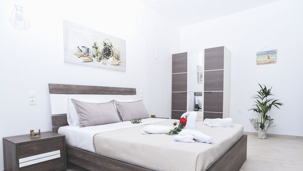 A modern bedroom with a wooden bed, a nightstand, a bedside table, a large mirror, and a potted plant. - Albertos House (Skiathos)