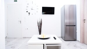 A modern kitchen with a white countertop, a stainless steel refrigerator, a wall-mounted TV, and a door with an emergency exit sign. - Albertos House (Skiathos)