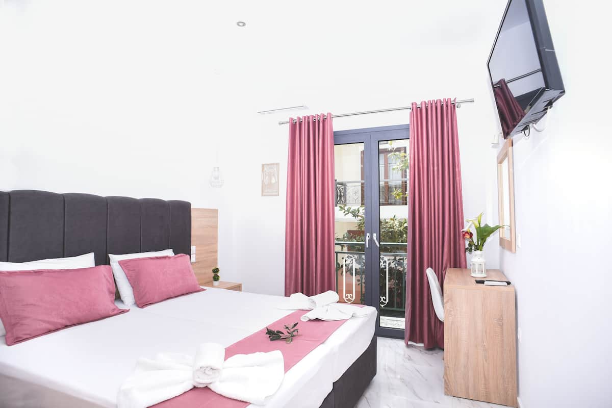 Habitación de hotel con cama, escritorio, televisor y balcón con cortinas.