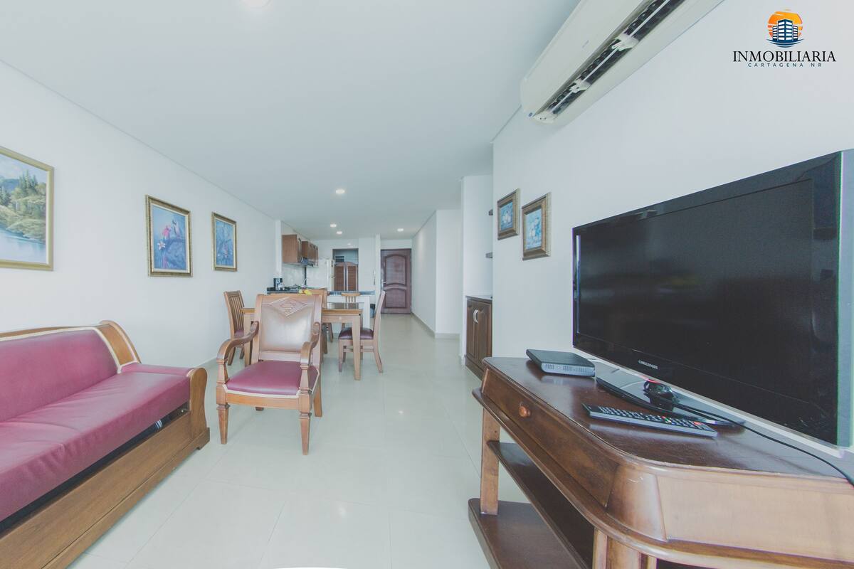 A living room with a sofa, chairs, a flat-screen TV, and framed pictures on the walls.