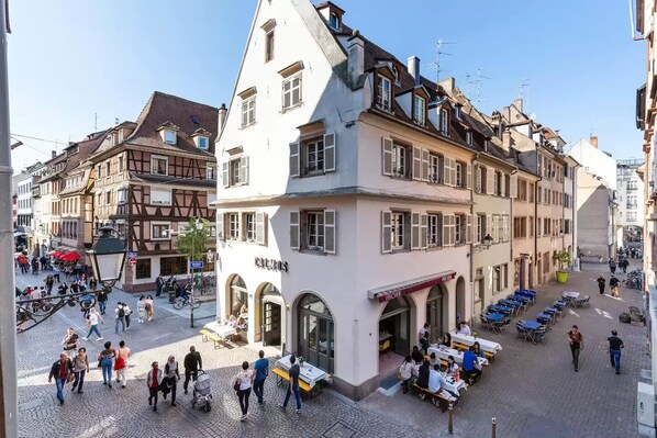 A historic building with a café on the ground floor, outdoor seating, and a cobblestone street.