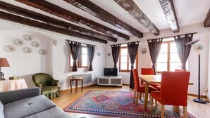 Een woonkamer met een bank, een eettafel met stoelen, een televisie en een kamerbreed tapijt.
