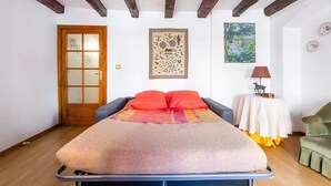 Een slaapkamer met een bed, een houten deur, een lijst met een afbeelding, een tafel met een lamp en een stoel.