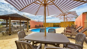 An outdoor pool area with lounge chairs, a table, and striped umbrellas. - Osprey Holiday Village Unit 111 - Villa with a Pool in the Complex (EXMOUTH)
