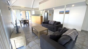 A modern living room with a sofa set, a coffee table, and a dining area with chairs and a table. - Osprey Holiday Village Unit 111 - Villa with a Pool in the Complex (EXMOUTH)