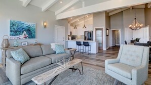 A spacious living area with a sofa, armchair, and a coffee table. A kitchen is visible in the background with a bar area. - Ocean front, rock view: Salty Sister 3Bdrm with outdoor patios to gather (Morro Bay)