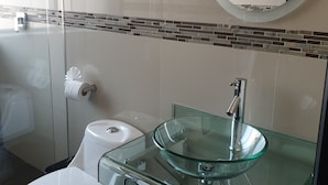 Une salle de bain moderne avec un lavabo en verre, des toilettes blanches et une douche à parois de verre.