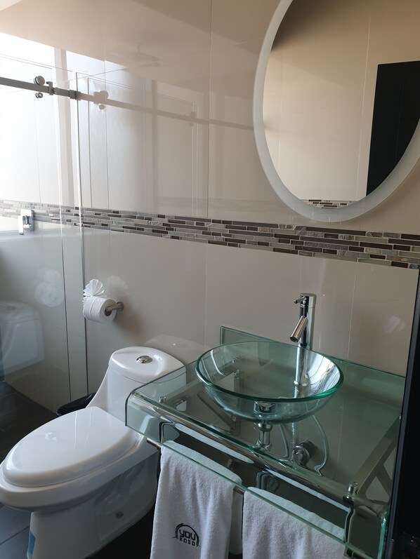 Une salle de bain moderne avec un lavabo en verre, des toilettes blanches et une douche à parois de verre.