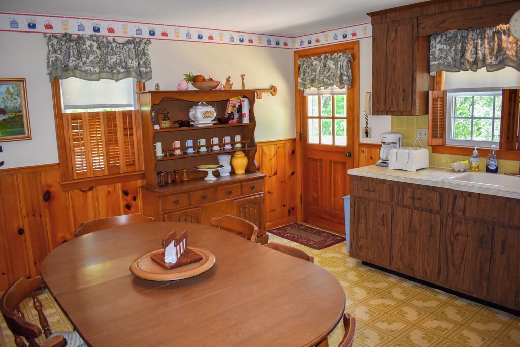 Un comedor de madera con una mesa redonda y sillas, una cocina con armarios de madera y una encimera, y una ventana con vistas a la vegetación.