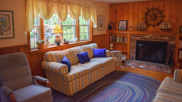Ein gemütliches Wohnzimmer mit einem gestreiften Sofa, einem Kamin und einer Holzwand mit einer Schiffslaugendekoration.