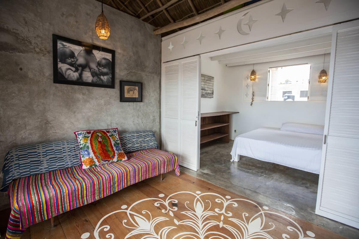 Una habitación con piso de madera, un sofá colorido a rayas, una cama blanca y un armario.