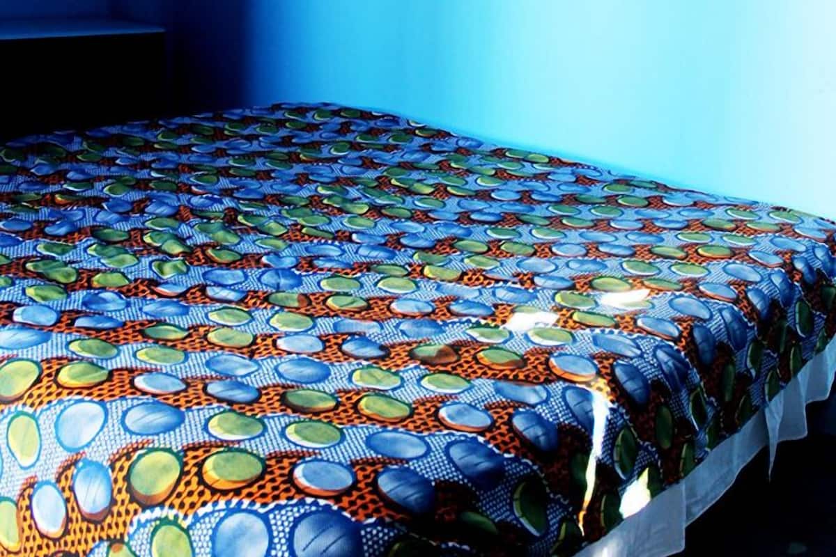 Una habitación con una colcha estampada, un adorno en la pared y un ventanal con perforaciones en forma de estrella.
