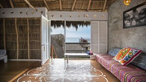 Una habitación con piso de madera, un sofá colorido, un banco y vista al mar a través de un ventanal.