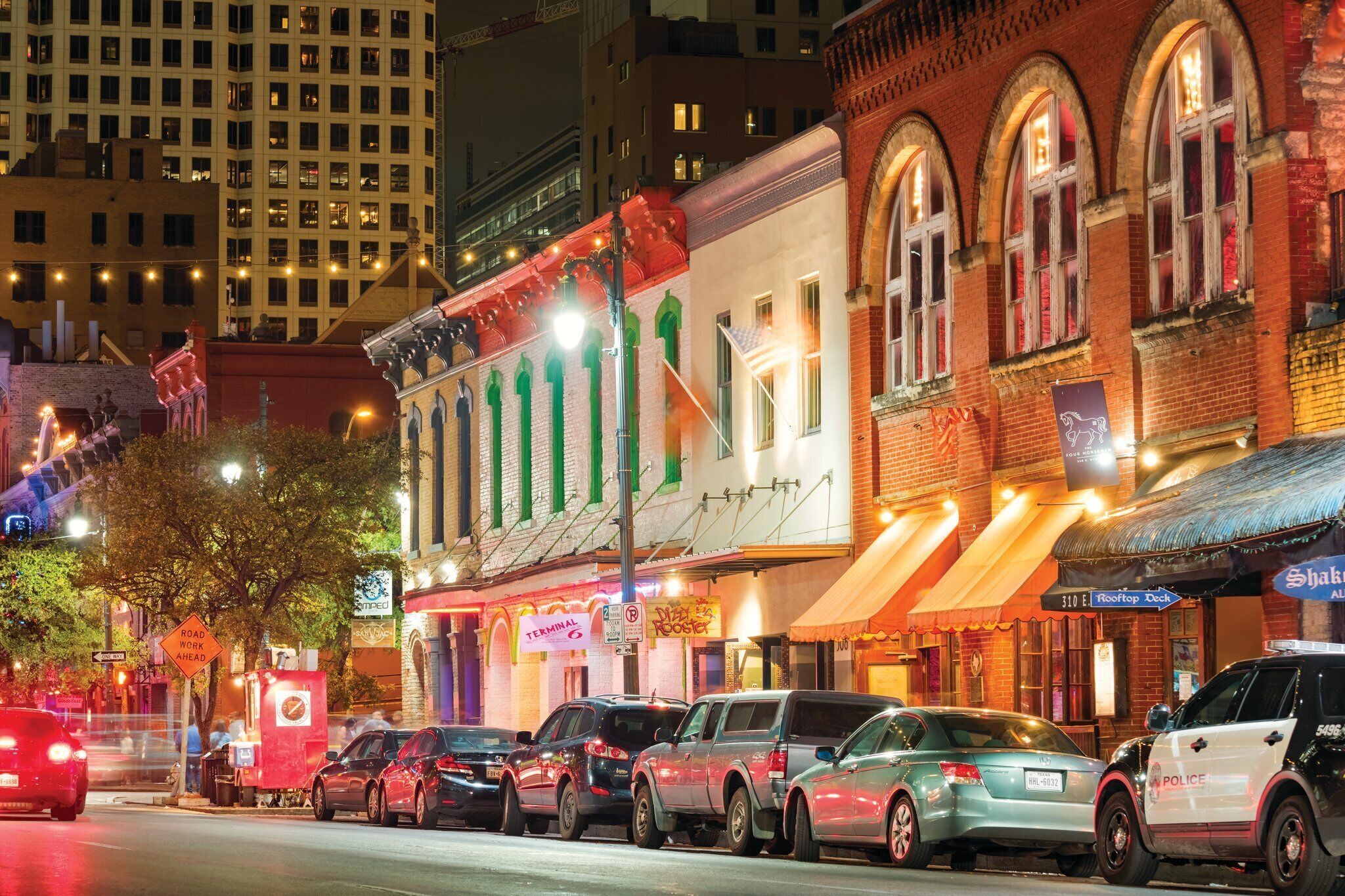A street lined with parked cars and buildings with various signs and storefronts.