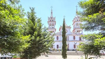 Una iglesia blanca con dos torres y un campanario central, rodeada de árboles.
