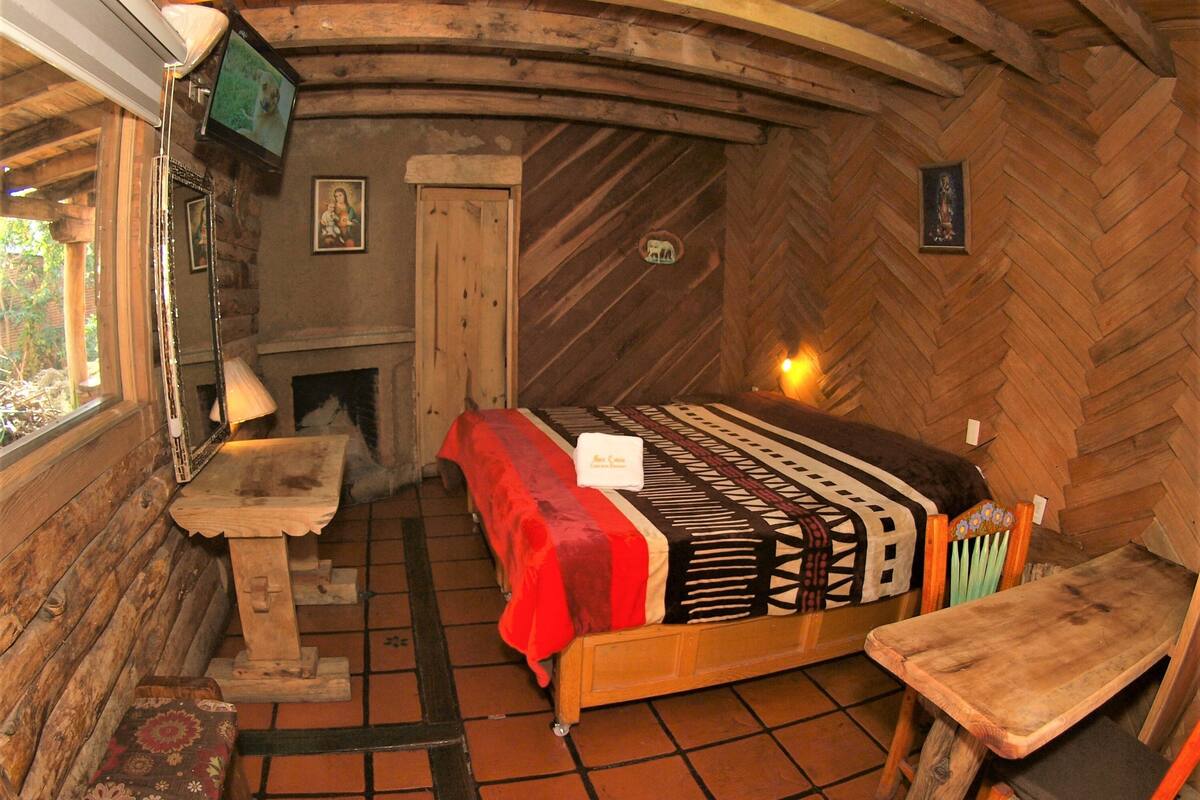 Une pièce rustique en bois, avec un lit, une petite table, une chaise, une cheminée et un téléviseur fixé au mur.