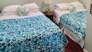 A room with two beds, each with a floral bedspread, a bedside lamp, and a window with blinds. - Fabulous 2 Bed, 2 Bath Cottage On Kangaroo Lake (Baileys Harbor)