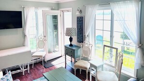 A bright room with a TV, a desk, and a chair. There are curtains on the windows, and a sign with a quote is on the wall. - Fabulous 2 Bed, 2 Bath Cottage On Kangaroo Lake (Baileys Harbor)