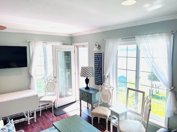 A bright room with a TV, a desk, and a chair. There are curtains on the windows, and a sign with a quote is on the wall.