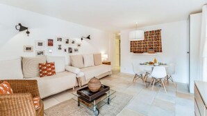 Un salon moderne avec un canapé, une table basse en verre et un coin repas comprenant une table et des chaises blanches.