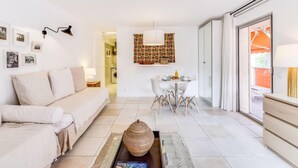 Un salon moderne avec un canapé, une table basse et un coin repas. On y trouve un luminaire fixé au mur et une décoration murale à motifs.