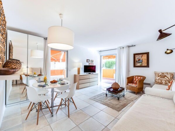 A modern living room with a dining area, a TV, and a large window. - Les Patios by Interhome (Saint-Tropez)