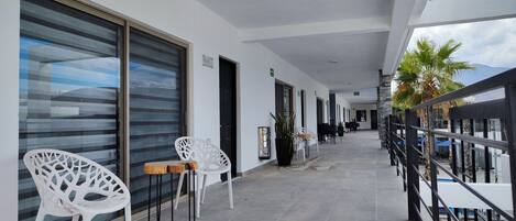 Un pasillo con sillas blancas, una mesa de madera y plantas en macetas.