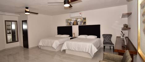 Habitación de hotel con dos camas, ventilador de techo, aire acondicionado, una silla y una pequeña mesa.