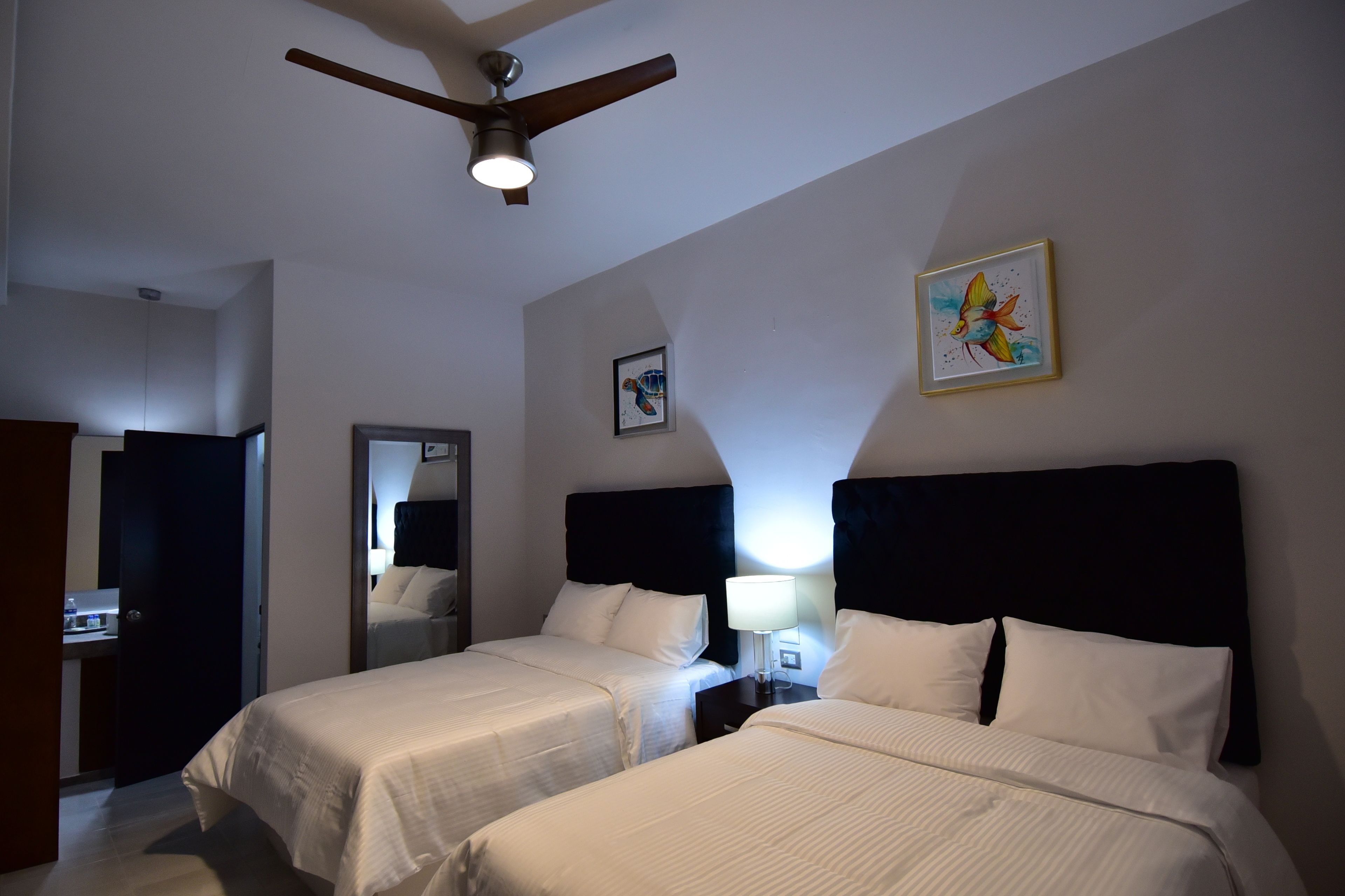 Una habitación de hotel con dos camas, ventilador de techo y obras de arte en las paredes.
