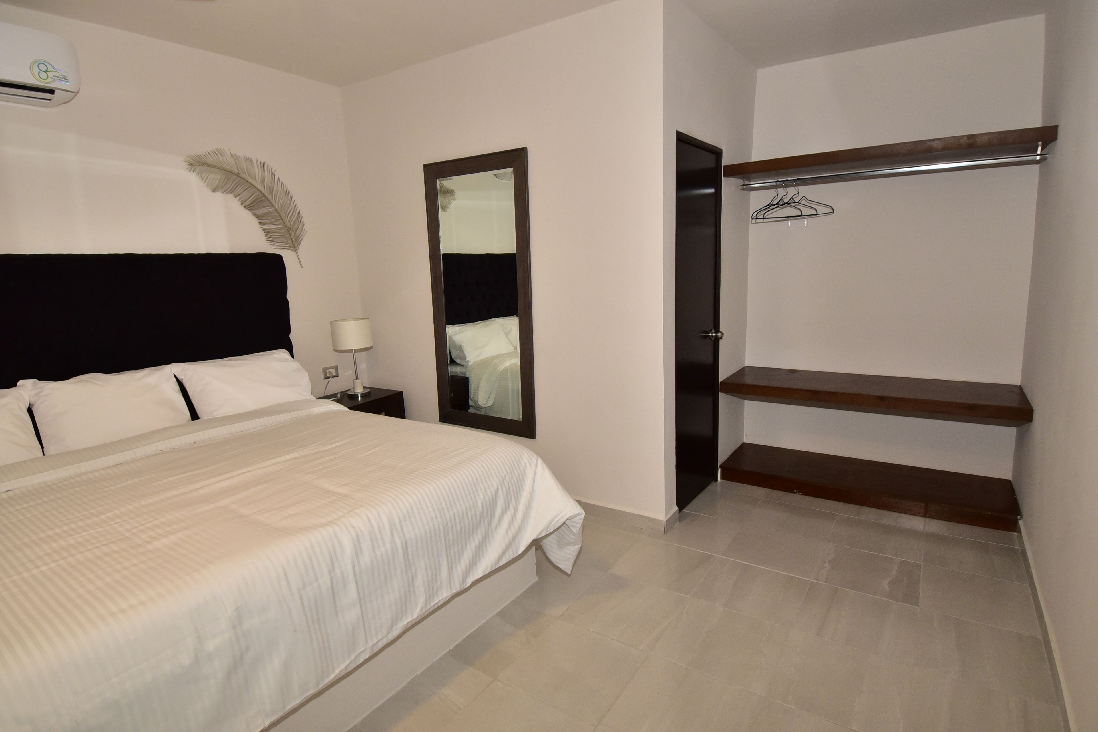 A bedroom with a bed, a nightstand, a mirror, a wardrobe, and a hanging coat rack.