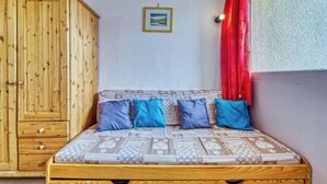 Un lit en bois avec une literie à motifs et des oreillers bleus, une armoire en bois et un rideau rouge.