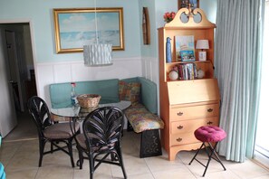 A living room with a teal sofa, a wooden bookcase, a dining table with chairs, and a pink stool. - Ocean View from the Balcony! (Rehoboth Beach)