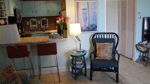 A kitchen with blue cabinets, a dining area with two red chairs, a black chair with a colorful cushion, and a small table with a lamp and books. - Ocean View from the Balcony! (Rehoboth Beach)