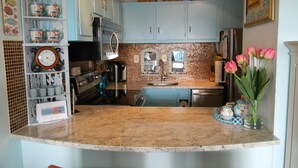 A kitchen with light blue cabinets, a granite countertop, a sink, and a stove. There are decorative items on the shelves and a vase with flowers on the counter. - Ocean View from the Balcony! (Rehoboth Beach)