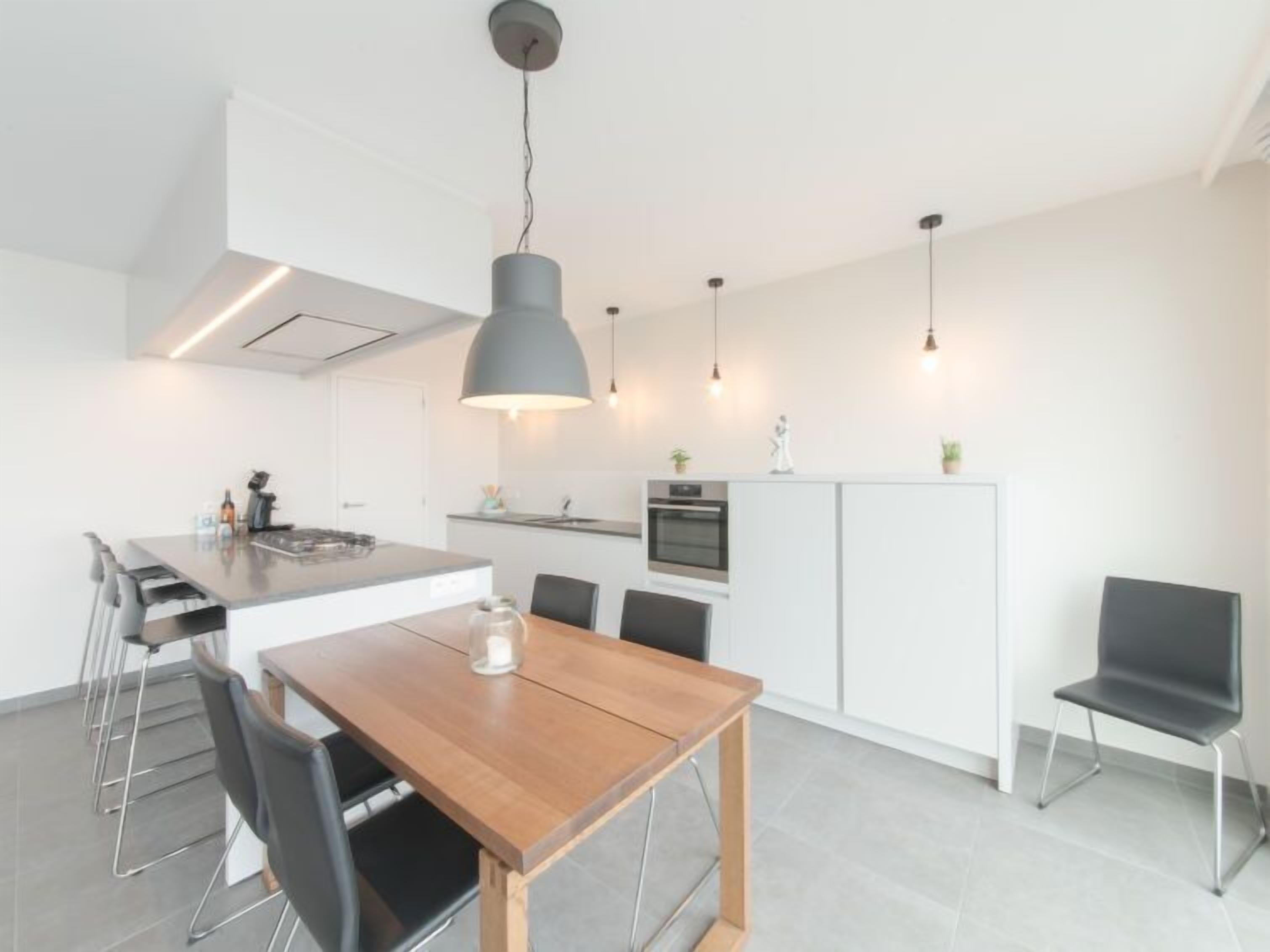 A modern kitchen with a central island, a dining table with chairs, and pendant lighting.