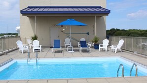 A rooftop pool with white lounge chairs and a blue umbrella.